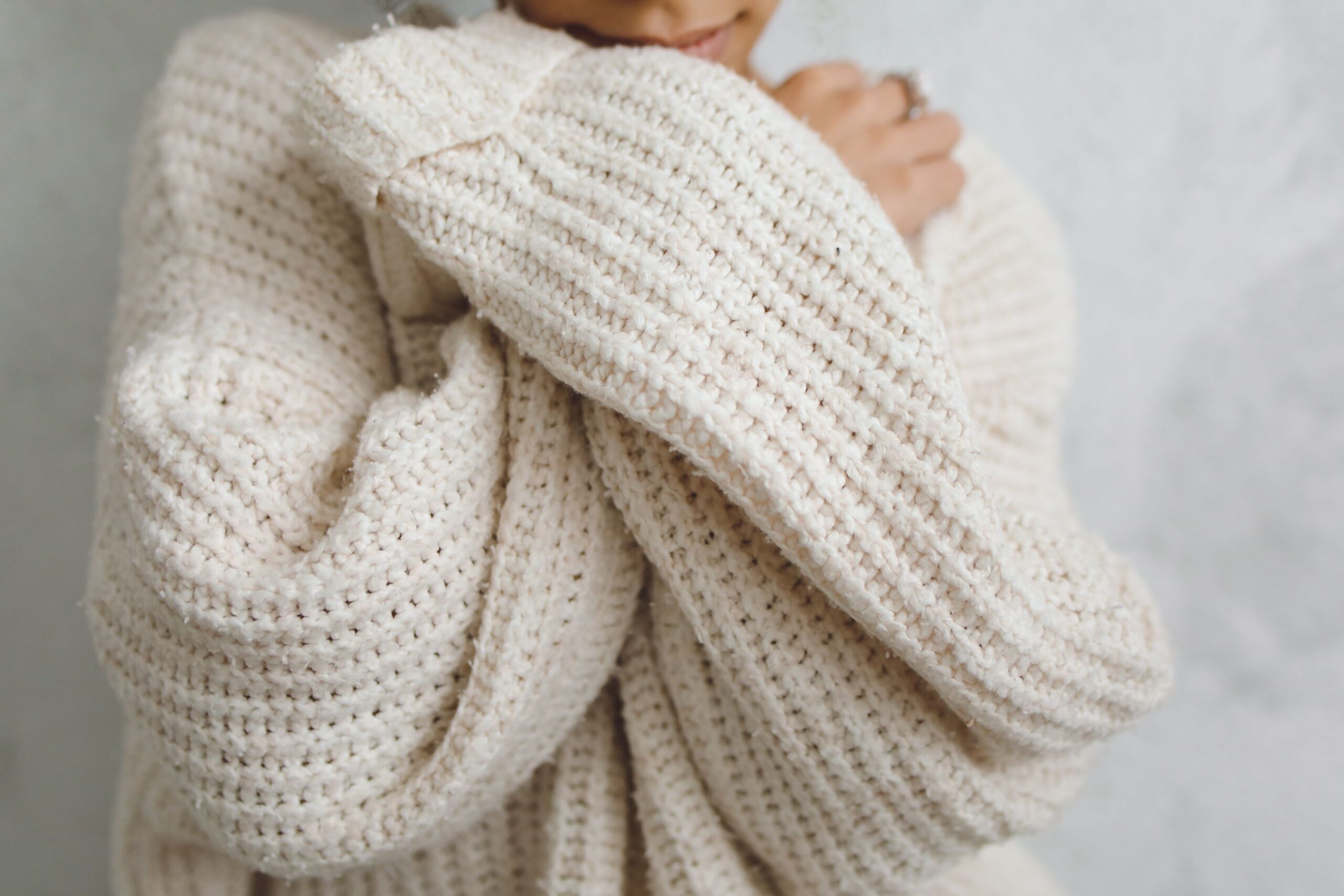 A close-up portrait of a person in a white knitted sweater with long sleeves, offering a warm and cozy feel.